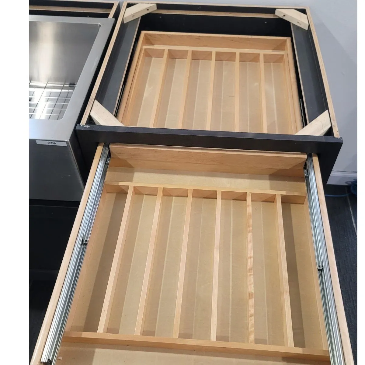 Top-down view of a double cutlery drawer with upper tray and lower storage compartment in a dark shaker base cabinet