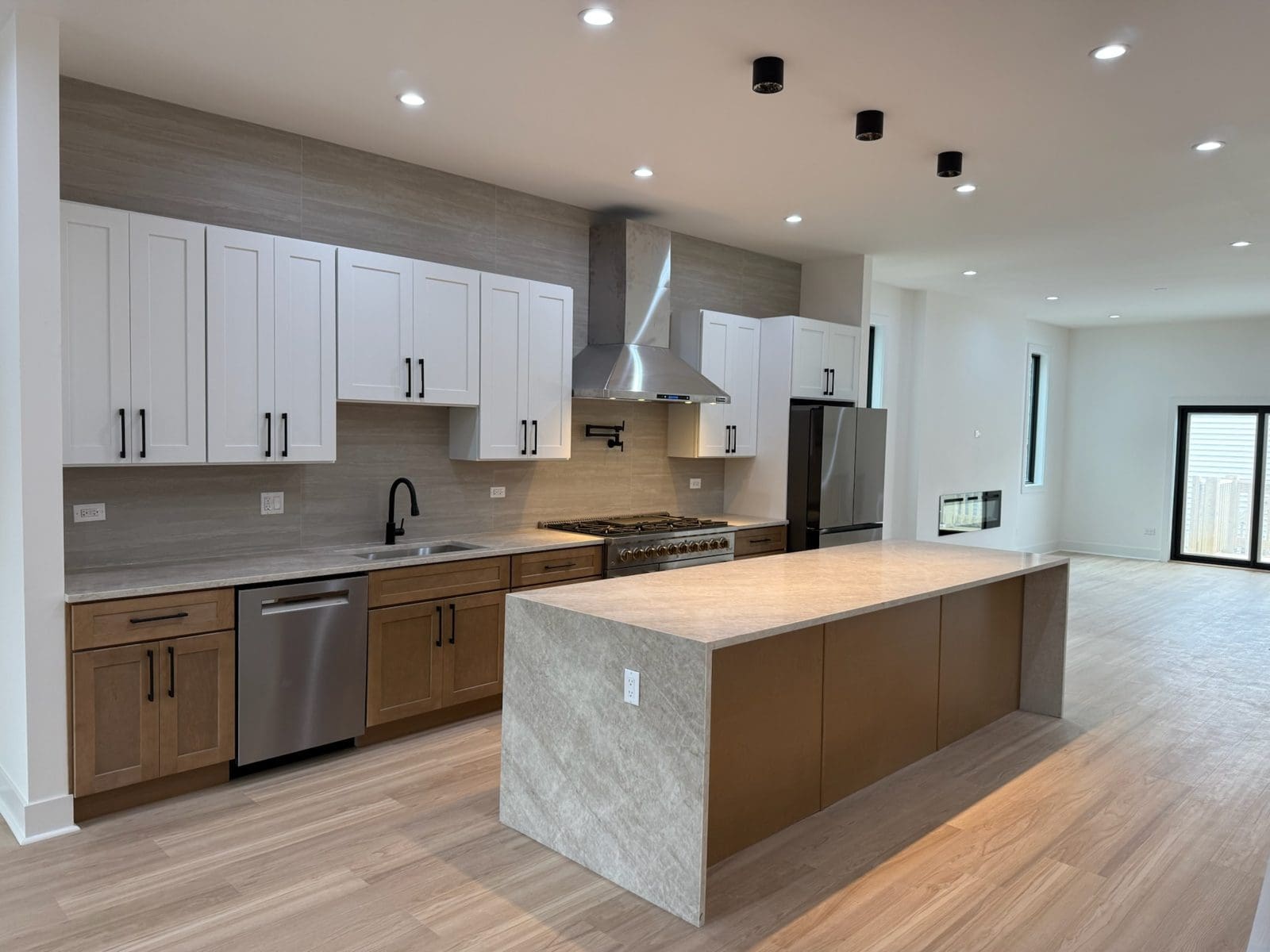 Two-tone shaker kitchen with white upper cabinets and natural oak base cabinets and a waterfall quartz island in a Woodlawn, Chicago new construction home
