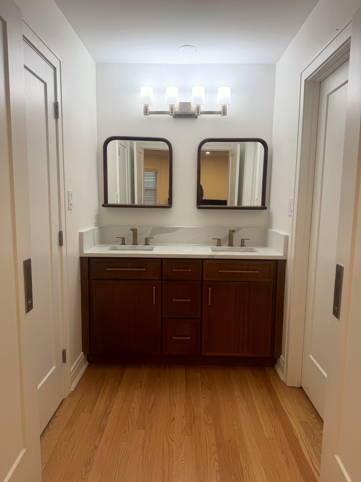 Dark-stained shaker double vanity with a centre three-drawer stack between two door cabinets, white quartz countertop, two undermount sinks, twin dark-framed mirrors and a four-light brushed nickel fixture in a Morton Grove, IL bathroom