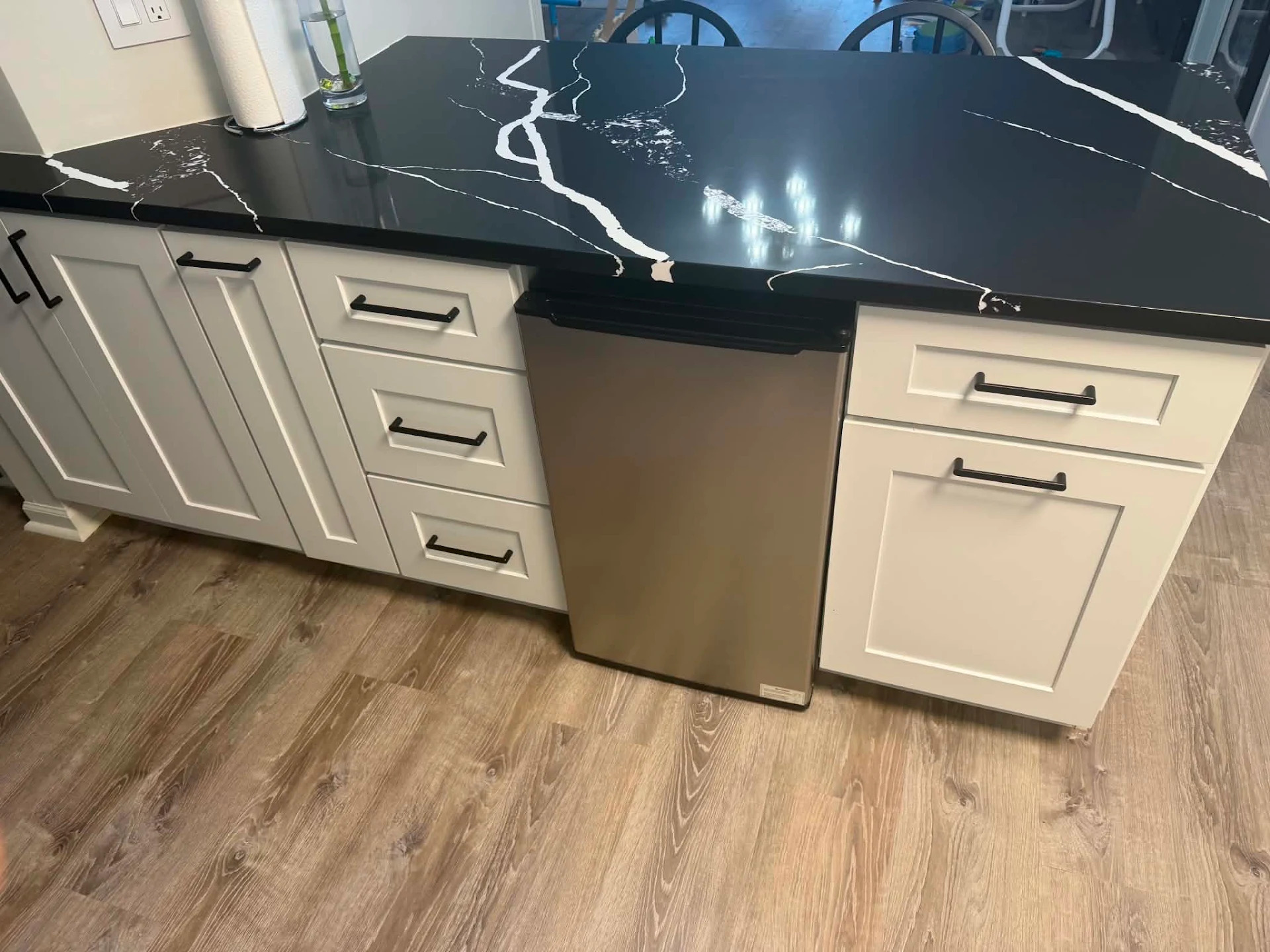 Installed black quartz countertop with bold white veining on a white shaker peninsula in a Norridge, IL kitchen, the polished slab overhanging a run of shaker drawer banks and a stainless dishwasher panel above wide-plank oak-look flooring