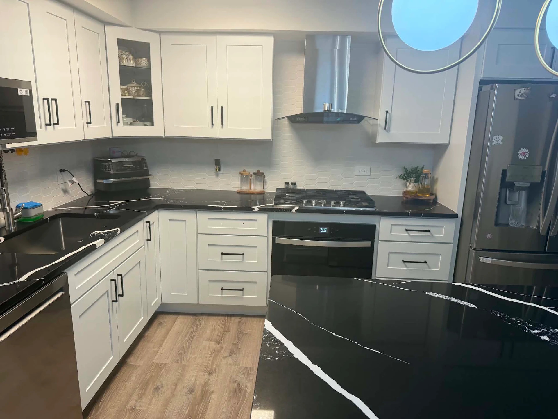 Black quartz countertop with white veining running the full cooktop wall of a Norridge, IL kitchen, wrapping the five-burner gas cooktop and built-in wall oven between white shaker cabinets with matte black bar pulls and a white hexagon tile backsplash