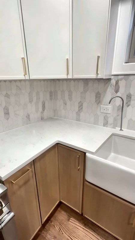 Two-tone slim shaker kitchen corner in Chicago: white-oak lower cabinets with brass pulls under Dove White slim shaker upper cabinets, beside a farmhouse sink base.